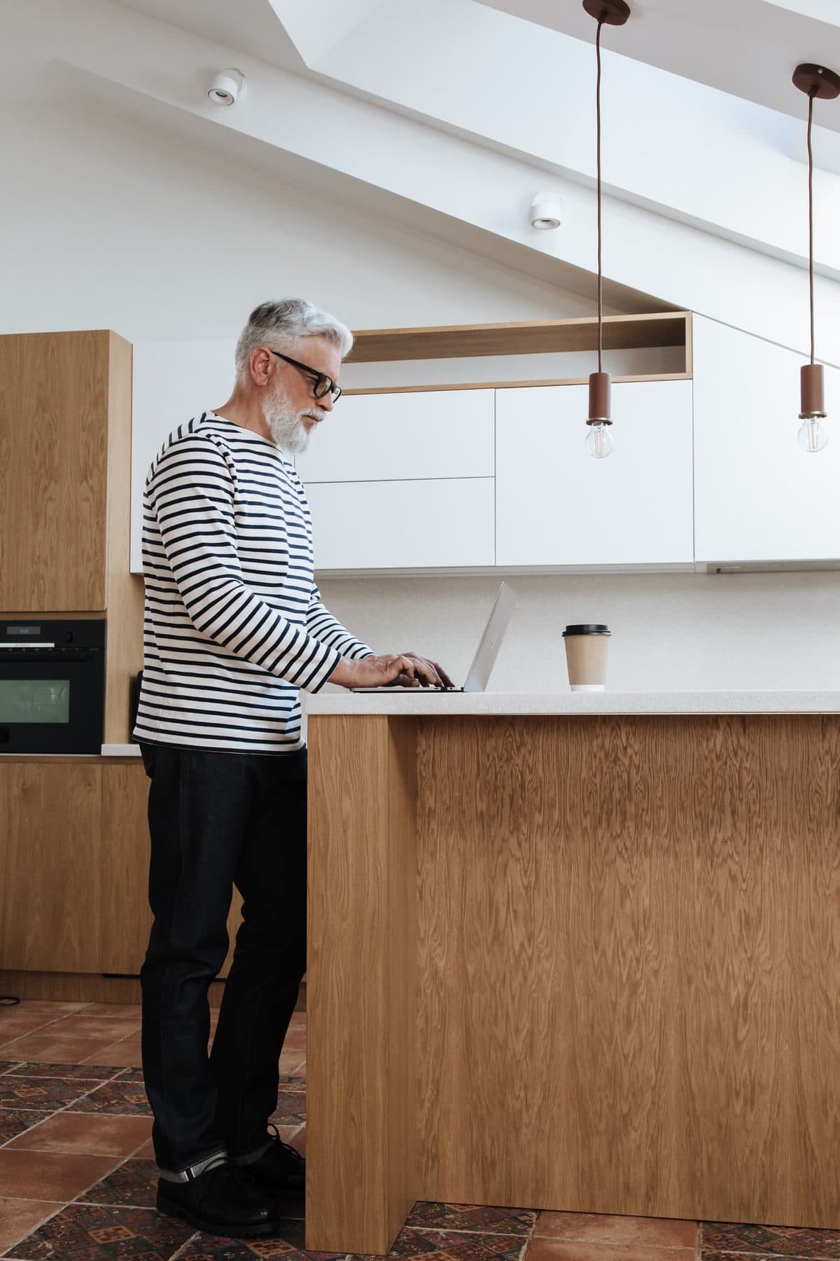 Man standing at a kitchen island using a laptop as a standing desk