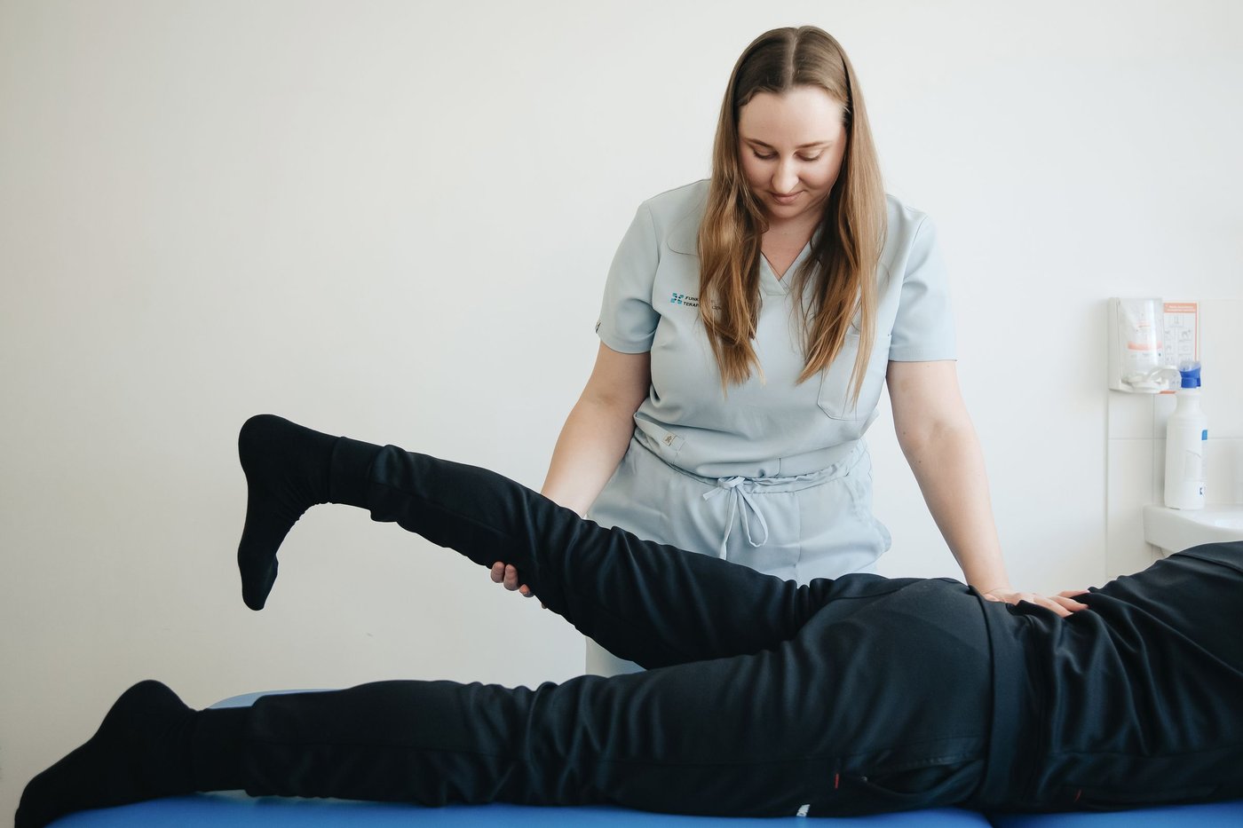 Physiotherapist guiding a patient through a leg and hip stretch on a treatment table
