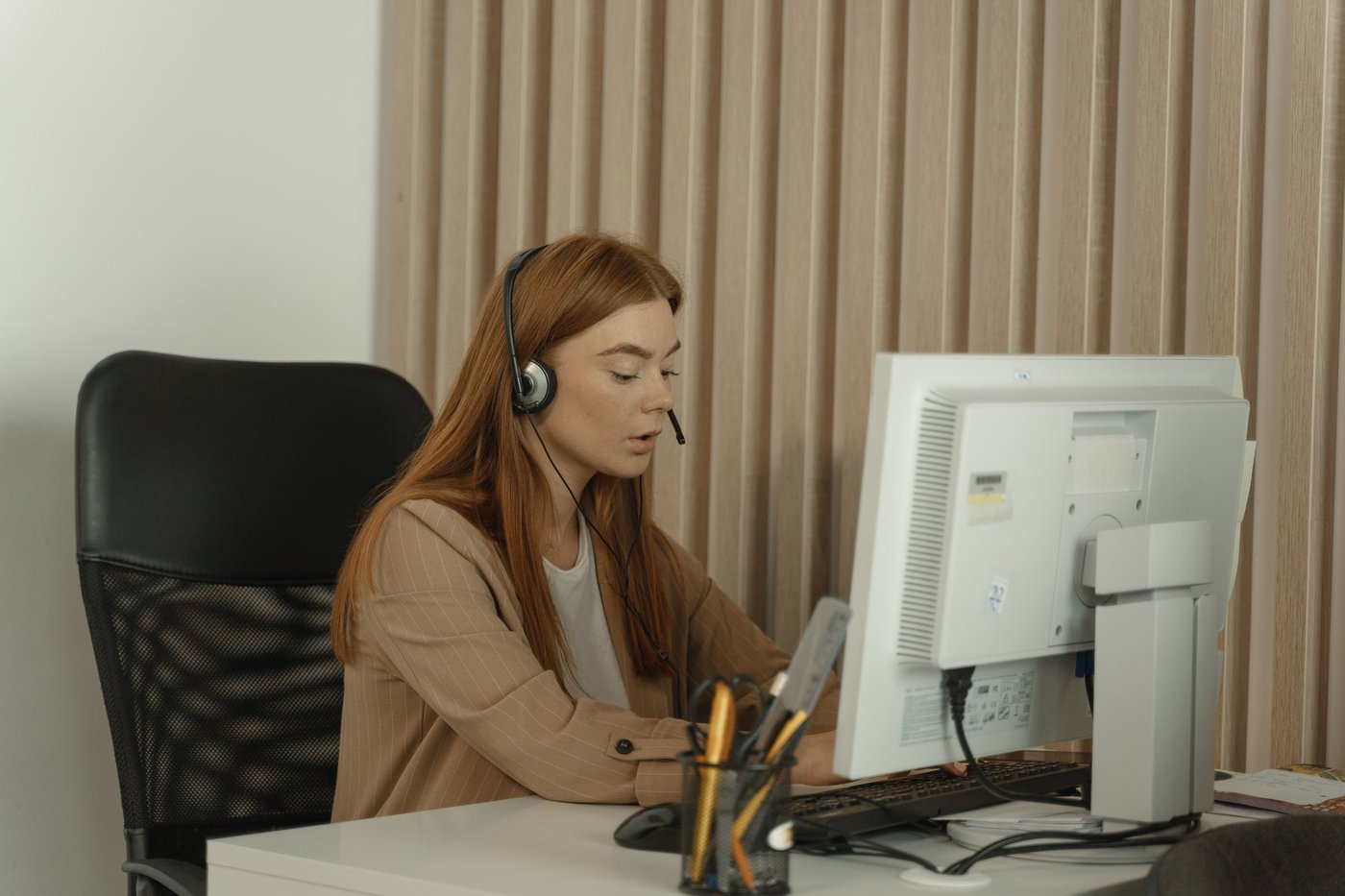 Woman with a headset working at a desktop computer in an office, seated for a long stretch