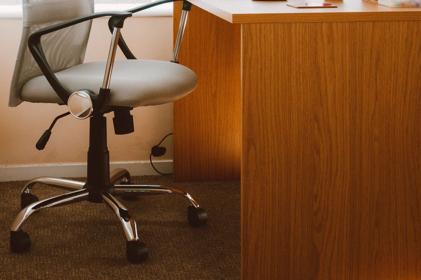 Grey office chair with a gas-lift height lever and fixed armrests beside a wooden desk