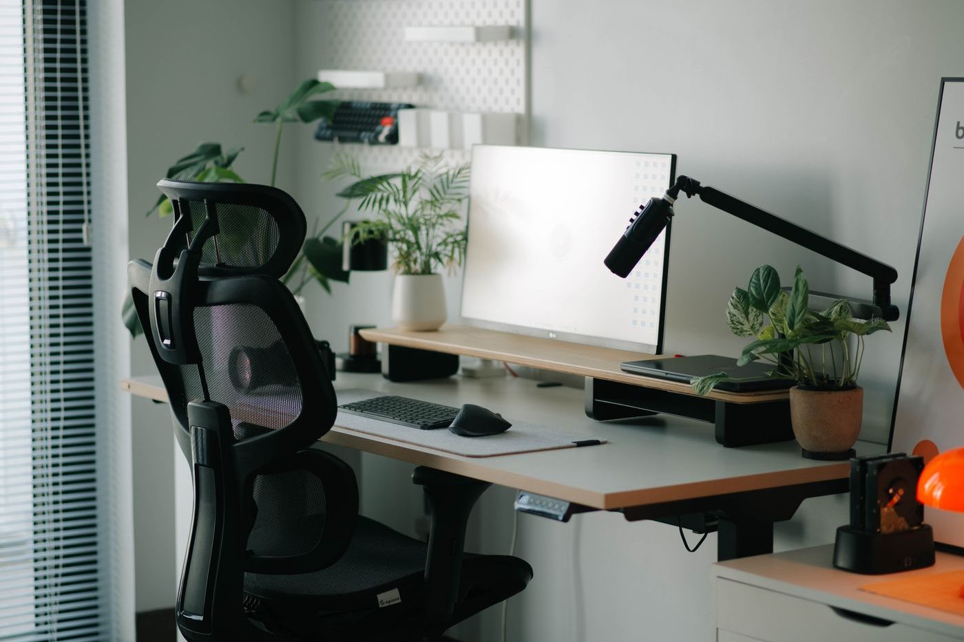 Black ergonomic office chair with a headrest pulled up to a height-adjustable desk in a bright home office