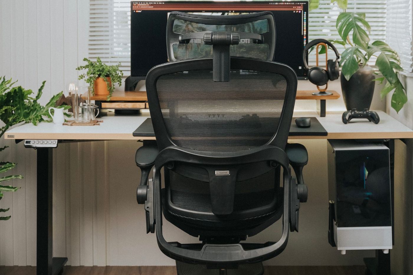 Black mesh ergonomic office chair with a headrest, curved backrest and adjustable armrests at a desk