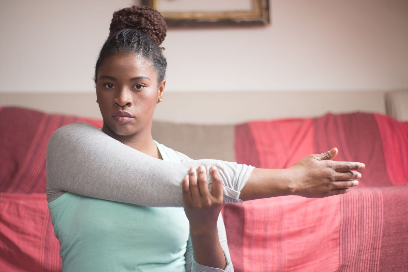 Woman on a sofa pulling one arm across her chest in a cross-body shoulder stretch