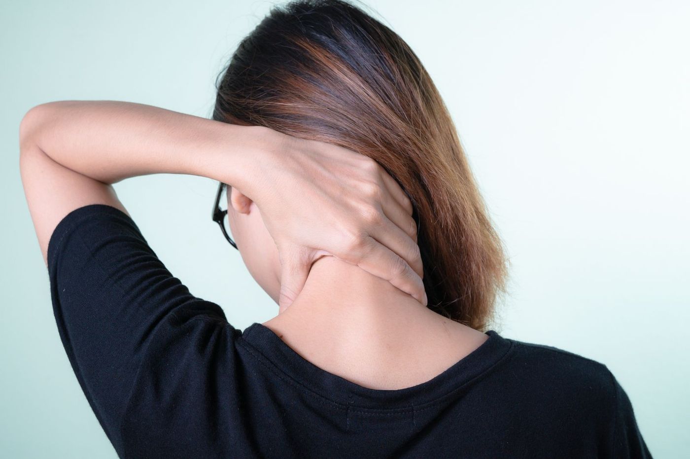 Woman seen from behind with one hand on the back of her neck and upper back, as if easing stiffness