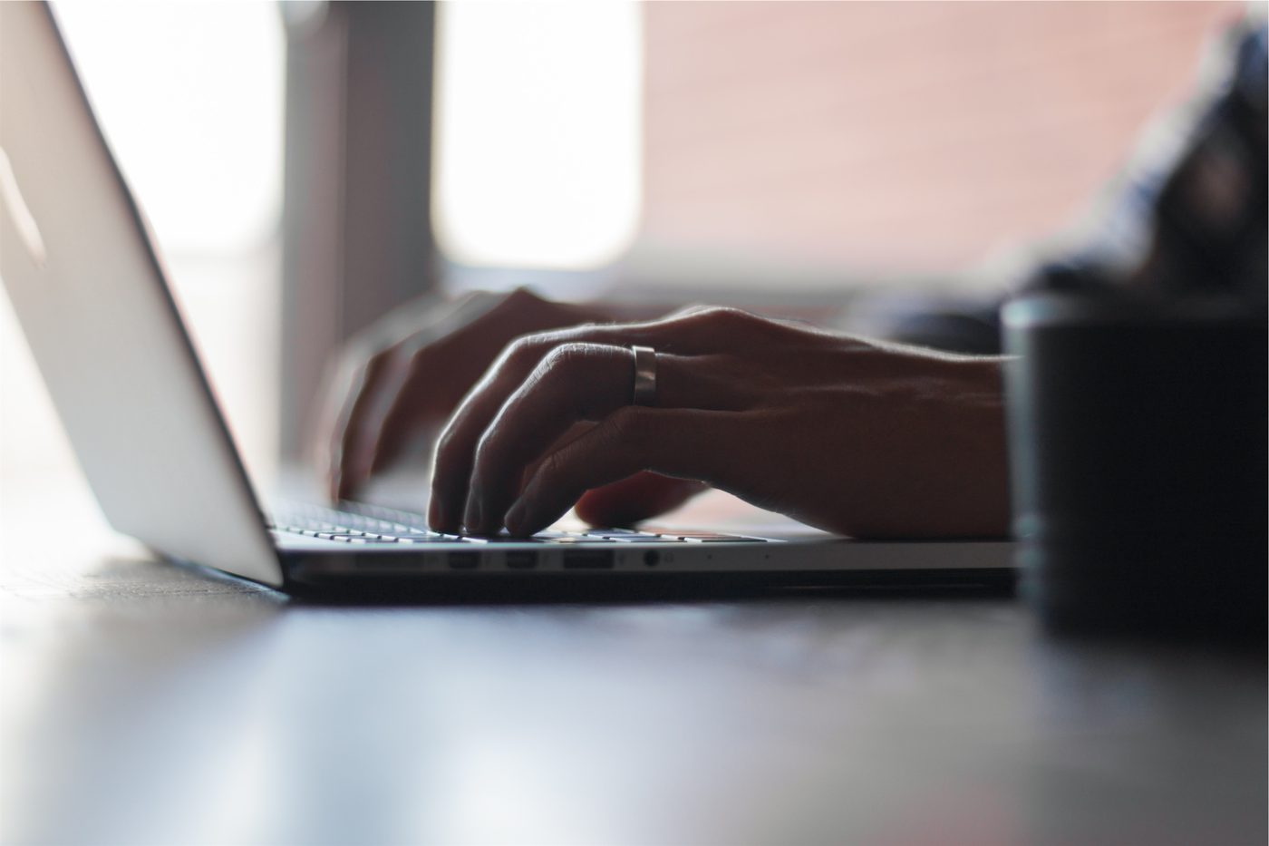 Hands typing on a laptop keyboard, seen from the side