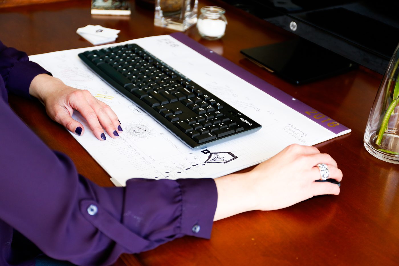 Woman typing on a black keyboard on a wooden desk
